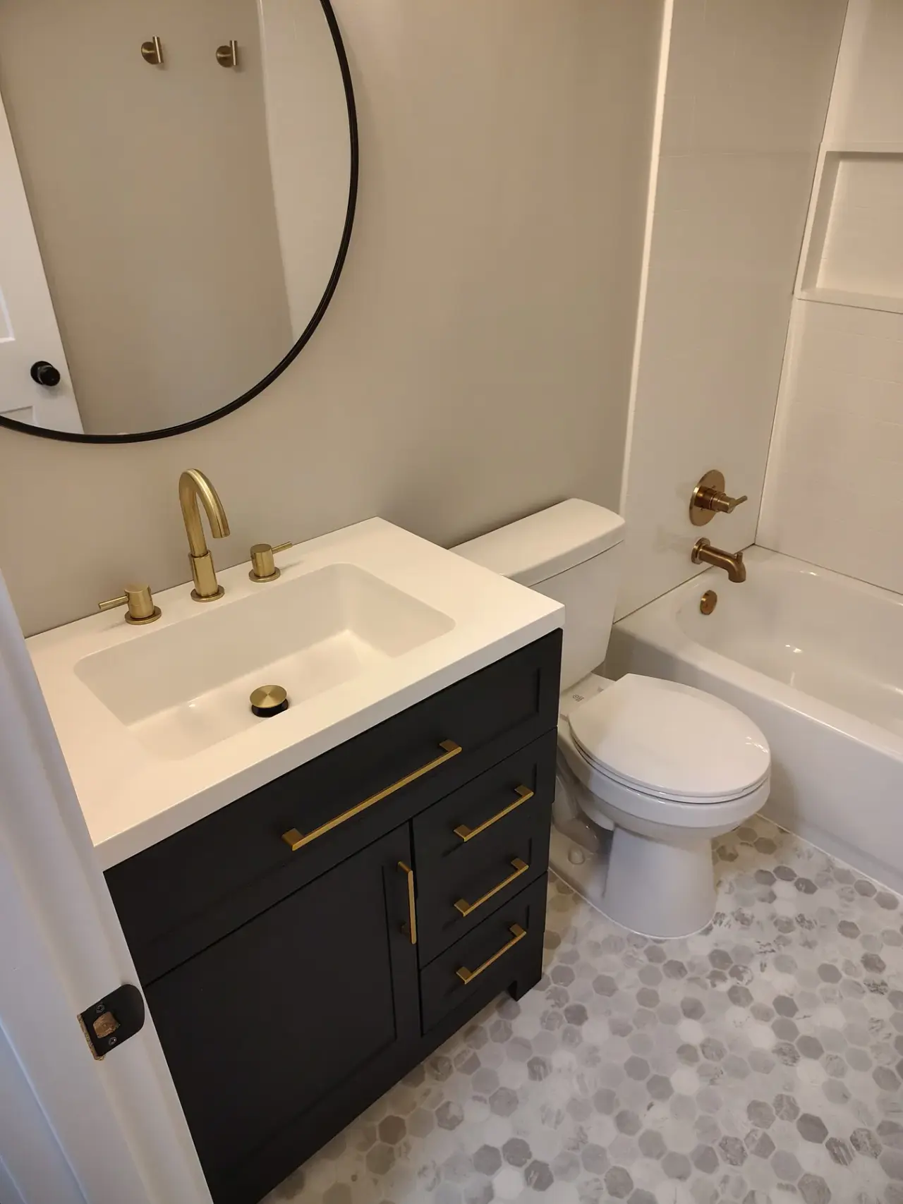 Renovated bathroom with black vanity, gold fixtures, and tiled floor